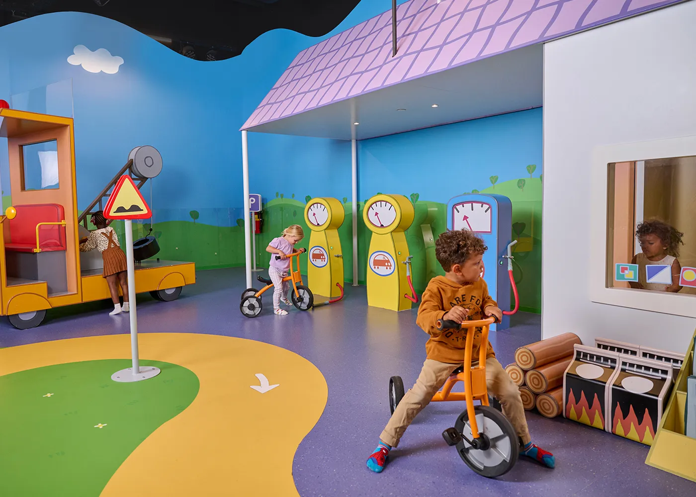 At PEPPA PIG World of Play in Chicago, young children play in Grandad's Garage, a colorful interactive area featuring a pretend gas station and a Peppa Pig-themed bus in a fun indoor setting.